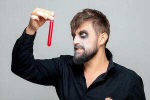 ein bärtig Mann mit Untote bilden zum Halloween hält Prüfung Röhren im welche rot Flüssigkeit foto