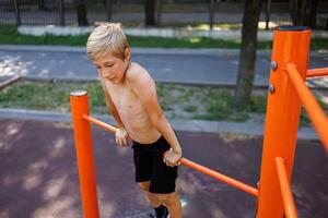 sportlich Teenager hält seine Gewicht auf das horizontal Bar. Straße trainieren auf ein horizontal Bar im das Schule Park. foto