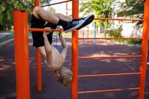 das sportlich Teenager gemacht ein Rückbeuge, hängend auf das horizontal Bar. Straße trainieren auf ein horizontal Bar im das Schule Park. foto