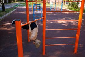 ein sportlich Kind gefangen seine Hände auf das horizontal Bar und gebogen zurück. Straße trainieren auf ein horizontal Bar im das Schule Park. foto