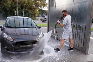 das Mann Ziele das Wasser Kanone beim das Autos Vorderseite Scheinwerfer und wäscht ihnen. ein Auto beim ein selbst Bedienung Auto waschen. foto