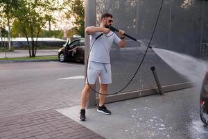 ein Mann hält ein Wasser Kanone zu waschen Autos ein Auto beim ein selbst Bedienung Auto waschen. foto