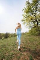 ein Aussicht von ein Mädchen von sportlich bauen Laufen durch das Park. schön blond kaukasisch Frau im Blau fest Trainingsanzug. blond Mädchen beim ein draussen Ausbildung Session foto