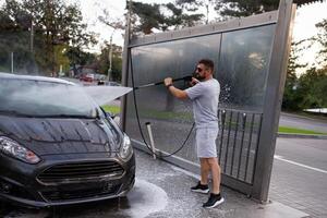 ein Mann beim das Auto waschen Punkte ein Wasser Kanone beim das Windschutzscheibe. ein Auto beim ein selbst Bedienung Auto waschen. foto