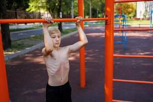 Teen mit Sport Muskel Entwicklung hält auf zu das Bar Straße trainieren auf ein horizontal Bar im das Schule Park. foto