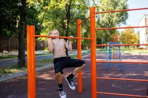 das Teenager ist schwer gezogen aus auf das Querlatte. Straße trainieren auf ein horizontal Bar im das Schule Park. foto