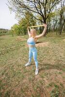 sportlich Mädchen Arbeiten aus im das Park Dehnen ein Gummi Band Über ihr Kopf. schön blond kaukasisch Frau im Blau fest Trainingsanzug. blond Mädchen beim ein draussen Ausbildung Session foto