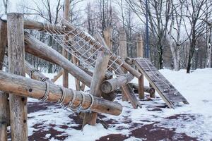 hölzern Spielplatz gemacht von natürlich umweltfreundlich Material im Öffentlichkeit Stadt Park mit Schnee beim Winter Zeit. modern Sicherheit Kinder draussen Ausrüstung. Winter Aktivitäten. Kinder sich ausruhen und Spiele auf öffnen Luft foto