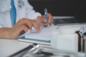 ein Fachmann und konzentriert asiatisch weiblich Arzt im Peelings ist Arbeiten und lesen medizinisch Forschung auf ihr Laptop im ihr Büro beim ein Krankenhaus. foto