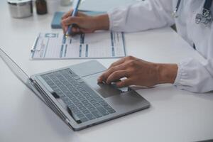 ein Fachmann und konzentriert asiatisch weiblich Arzt im Peelings ist Arbeiten und lesen medizinisch Forschung auf ihr Laptop im ihr Büro beim ein Krankenhaus. foto