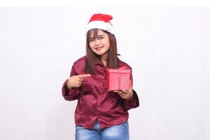 Porträt von ein Schön, heiter asiatisch Mädchen im ihr 20er Jahre Tragen verpackt Geschenke beim Weihnachten, Santa claus Hut, modern glänzend rot Shirt, zeigen Geschenke auf ein Weiß Hintergrund zum Beförderung und Werbung foto