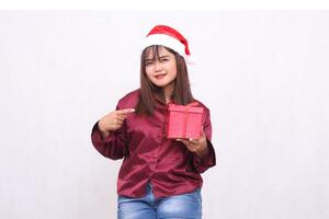 Foto Porträt von ein schön elegant asiatisch Mädchen im ihr 20er Jahre Tragen verpackt Geschenke beim Weihnachten Santa claus Hut tragen glänzend modern rot Hemd zeigen Geschenke auf ein Weiß Hintergrund zum Beförderung