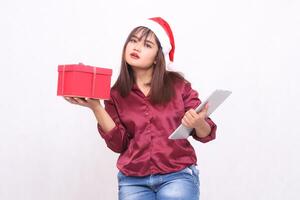 schön jung elegant Süd-Ost asiatisch Frau bringen Geschenk Korb und Tablette Laptop beim Weihnachten tragen Santa Hut modern rot Hemd Outfit Weiß Hintergrund zum Beförderung und Werbung foto