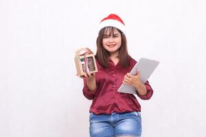 schön jung Süd-Ost asiatisch Frau lächelnd bringen Essen Paket Geschenke im Korb und Laptop Tablette beim Weihnachten tragen Santa Hut tragen rot Hemd modern Weiß Hintergrund zum Werbung foto
