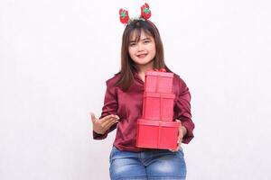 heiter jung schön Süd-Ost asiatisch Frau Einführung 3 Geschenk Kisten beim Weihnachten tragen Santa claus Stirnband und modern rot Hemd auf Weiß Hintergrund zum Beförderung und Werbung foto