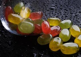 ein Menge von Süßigkeiten Stöcke sind verstreut von ein umgestürzt Glas Kelch. mehrfarbig Süßigkeiten im ein Glas auf ein schwarz Hintergrund. Marmelade Süßigkeiten. foto