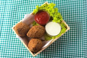 gebratener Kibbeh mit Tomatensauce im Korb, über rustikalem Holztisch foto