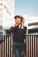 glückliche junge asiatische frau, die musik hört und spaß mit kopfhörern auf der straße hat foto