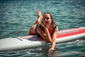 Frau Saft Meer. Sport Mädchen auf ein Surfbrett im das Meer auf ein sonnig Sommer- Tag. im ein schwarz Baden Anzug, er Lügen auf ein Saft im das Meer. sich ausruhen auf das Meer. foto