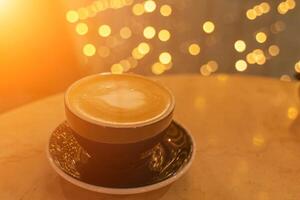 ein Tasse von Latté Kaffee mit herzförmig Schaum auf ein Tabelle im ein Cafe, im das Hintergrund, das Beleuchtung im ein verwischen sind reflektiert auf das Tisch. foto