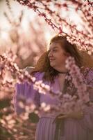 Frau Blühen Pfirsich Obstgarten. gegen das Hintergrund von ein malerisch Pfirsich Obstgarten, ein Frau im ein lange Rosa Kleid und Hut genießt ein friedlich gehen im das Park, umgeben durch das Schönheit von Natur. foto