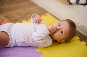 europäisch schön Baby Junge 6-8 Monate alt Lügen auf mehrfarbig Puzzle Teppich, Säugling seine Finger, suchen beim Kamera mit Neugier. schön Babys. Kindheit und Säuglingsalter. Kinder Wachstum und Entwicklung foto