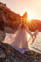 mysteriös Frau Silhouette lange Haar Spaziergänge auf das Strand Ozean Wasser, Meer Nymphe Wind hört zu zu das Welle. wirft oben ein lange Weiß Kleid, ein göttlich Sonnenuntergang. künstlerisch Foto von das zurück ohne ein Gesicht