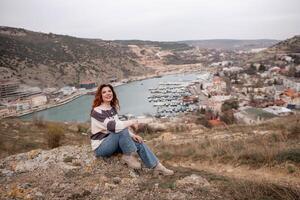 ein Frau ist Sitzung auf ein Felsen mit Blick auf ein Körper von Wasser. das Szene ist friedlich und heiter, mit das Frau suchen aus Über das Wasser und nehmen im das Sicht. foto