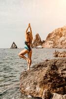 Yoga auf das Strand. ein glücklich Frau meditieren im ein Yoga Pose auf das Strand, umgeben durch das Ozean und Felsen Berge, fördern ein gesund Lebensstil draußen im Natur, und inspirierend Fitness Konzept. foto