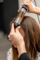 das Friseur bereitet vor ein Frau, macht ein Frisur mit Locken mit ein Eisstockschießen Eisen. lange Licht braun natürlich Haar. selbst Pflege Konzept. foto