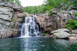 majestätisch Wasserfall Kaskadierung Nieder moosbedeckt Felsen in erfrischend Schwimmbad unten foto