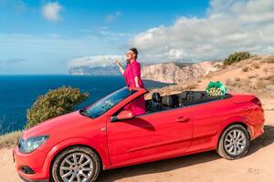ein Frau ist posieren auf oben von ein rot Wagen. sie ist tragen ein Rosa passen und Sonnenbrille. foto