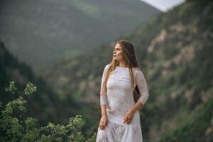 ein Frau im ein Weiß Kleid steht auf ein Berg oben foto