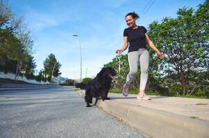 glücklich Frau lächelnd genießen Gehen ihr Hund draußen im das Natur. ziemlich weiblich sportlich Frau nehmen ihr Stammbaum schwarz Cocker Spaniel Hund zum ein gehen auf sonnig Tag foto