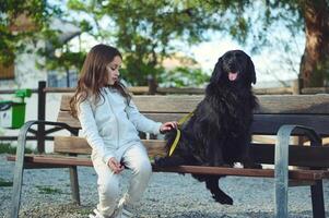 wenig Kind nd ihr Hund auf das Stadt Bank im das Natur draußen. süß Kind Gehen ihr Hund auf Leine foto