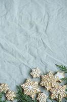 Fichtenzweige mit Weihnachtslebkuchenplätzchen auf dem grünen Leinen zerknitterten Textilhintergrund foto