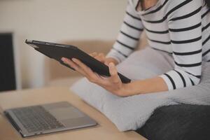 jung attraktiv asiatisch Frau ruhen mit Surfen Tablette Computer auf Sofa beim heim, glücklich Mädchen Sitzung auf Couch entspannen lesen Digital Gadget mit aufgeregt, Kommunikation und Lebensstil Konzept. foto