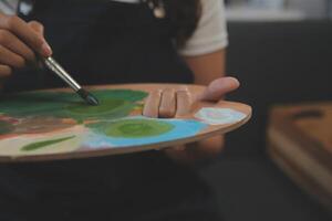 abgeschnitten Bild von weiblich Künstler Stehen im Vorderseite von ein Staffelei und Eintauchen Bürste in Farbe Palette foto