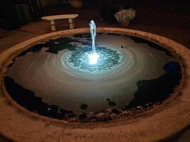 ein einfach Wasser Brunnen mit hell Beleuchtung beim Nacht im ein historisch Haus und Garten foto