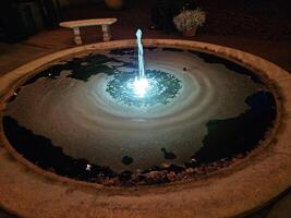 ein einfach Wasser Brunnen mit hell Beleuchtung beim Nacht im ein historisch Haus und Garten foto