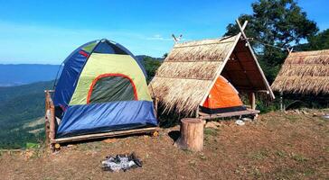 das Camping Blau, Grün und Orange Zelt auf hölzern Wurf mit trocken Blätter Dach und Blau Himmel, Berg und Baum Vordergrund im Sommer- Zeit. foto