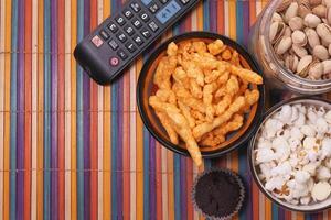 Popcorn, Koteletts im Schüssel und Fernseher Fernbedienung auf Tisch. foto