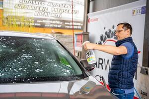 Prag, Tschechisch Republik - - April 5, 2024. jung Mann gilt Flüssigkeit zu sauber Fenster von das Auto im Selbstbedienung Auto waschen. hoch Qualität Foto