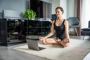 jung Frau im Sportbekleidung tun Yoga Übungen auf Matte im Leben Zimmer. online trainieren, Fitness, üben und Meditation beim Zuhause foto