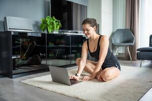 jung Frau im Sportbekleidung vorbereiten zu Fitness Übungen auf Matte im Leben Zimmer. online trainieren, üben und Meditation beim heim. foto