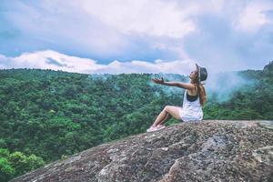 asiatische frauen reisen im urlaub entspannen. sitzen auf einer felsigen Klippe. wildes naturholz auf dem berg. foto