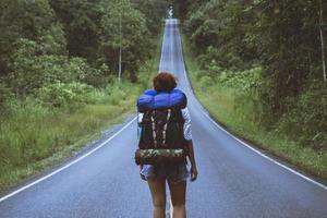 Freiheitsreisende Frau, die mit erhobenen Armen steht und eine schöne Natur auf einer Landstraße genießt. Frau mit Rucksack reisen auf dem Lande auf einem Berg. foto