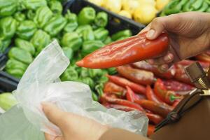 Frau Putten ein Paprika im ein Plastik Paket beim Super Geschäft foto