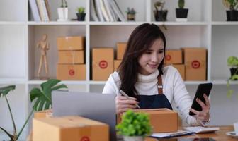 Versand online einkaufen, junge Start-up-Kleinunternehmer, die Adresse auf Karton am Arbeitsplatz schreiben. Kleinunternehmer KMU oder freiberufliche asiatische Frau, die zu Hause mit Box arbeitet foto