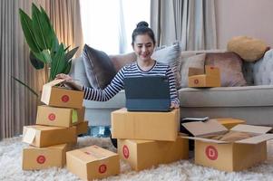 Online-Marketing, junge Start-up-Kleinunternehmer, die Adresse auf Karton aus Listenauftrag schreiben. Kleinunternehmer KMU oder freiberufliche asiatische Frau, die zu Hause mit Box arbeitet foto